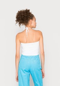 Top branco sem alças com um laço nas costas, combinado com calças de veludo cotelê azuis com dois bolsos traseiros e um corte largo.