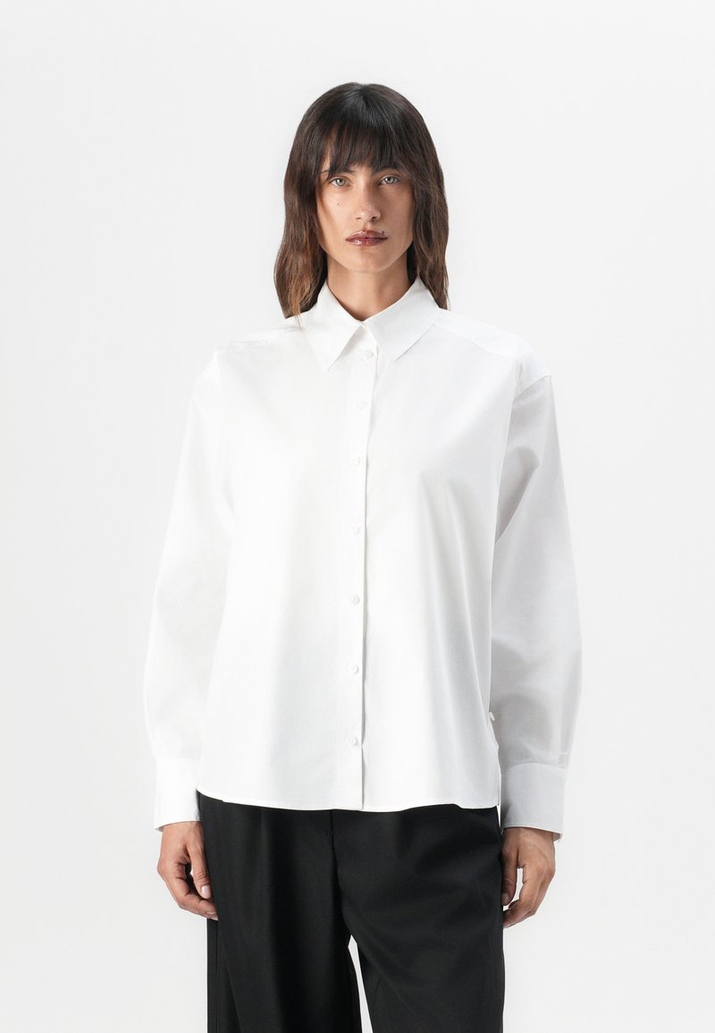 White long-sleeve button-up shirt with a pointed collar, made of smooth cotton fabric, featuring a relaxed fit and subtle shoulder seams.