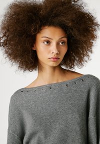 Pelēks ribots adījums džemperis ar plašu kakla izgriezumu, papildināts ar metāla acu caurumiem gar malu. Mīksta tekstūra un vaļīga piegriezuma forma ir izteikti elementi.