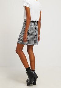Falda corta en blanco y negro de patrón houndstooth, con un tejido texturizado, cintura ajustada y forma de línea A, combinada con botas de ankle negras con tacón.