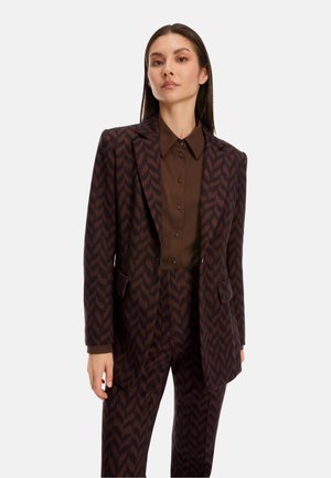Brown patterned blazer with matching trousers, featuring sharp lapels and front pockets, worn over a brown button-up shirt. Smooth texture.
