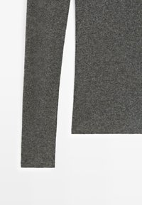 Manche longue d'un pull tricoté gris foncé avec un gros plan sur la texture du tissu sur fond blanc.