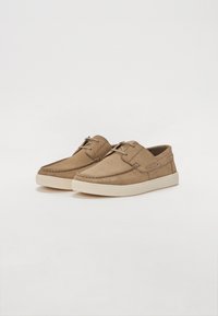 Pantofi din suede bej cu un design simplu, având vârful rotund, șireturi și o talpă din cauciuc de culoare deschisă. Textură netedă cu accente cusute.