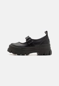 Black Mary Jane-style shoes with a chunky rubber sole, strap with buckle detail, glossy finish, rounded toe, and reinforced heel tab.