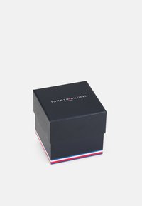 Scatola di cartone nero con un coperchio, con un logo bianco sopra. La base ha un accento a strisce rosse, bianche e blu.