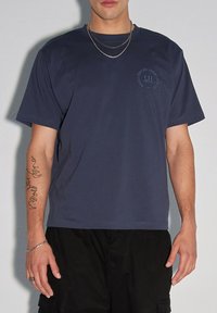 Granatowa bawełniana koszulka z krótkim rękawem, okrągłym dekoltem i okrągłym logo na lewej piersi. Gładka struktura i luźny krój.