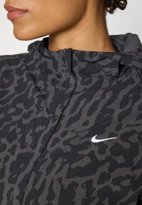 Nike jacket featuring a black and grey leopard print design, with a high collar, zipper closure, and a small white logo on the chest.