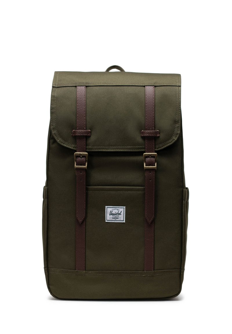 Grüner Stoff-Rucksack mit braunen Lederträgern, zwei vorderen Schnallen, einem oberen Klappenverschluss und einer kleinen Vordertasche mit einem Logopatch.