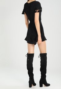 Mono de tela negra con mangas cortas y acentos de flecos. Se lleva con botas altas de ante negro y tacones cuadrados.