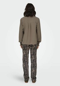 Maslinasto zelena bluzica dugih rukava s nabranom pozadinom, uparen s bež hlačama s leopard uzorkom. Oba odjevna komada imaju ležeran kroj i mekane teksture.