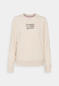 Beige crewneck sweatshirt med "TOMMY JEANS" broderat på framsidan, långa ärmar och en liten Tommy Hilfiger-flagglogga på vänster mudd.