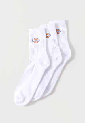 Trois paires de chaussettes blanches montantes avec bords côtelés et un patch logo Dickies coloré sur le côté extérieur près du haut.