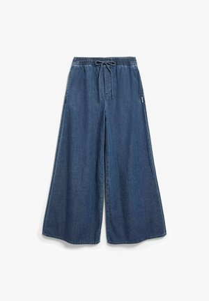 Blauwe denim broek met wijde pijpen, elastische tailleband en tunnelkoord, voornaaddetail en zijzakken, plat gelegd op een witte achtergrond.