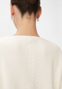 Weißer Strickpullover mit geripptem Textur und einem zentralen Zopfmuster-Detail entlang des Rückens. Rundhalsausschnitt mit lockerer Passform.