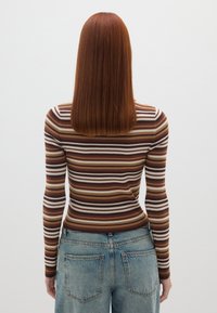 Gestreifter, gerippter Langarmoberteil in Braun, Creme und Rosttönen, kombiniert mit hellblauen Jeans. Glatte Textur mit tailliertem Design.