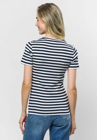 Svētku krekls ar svītrām jūras zilā un baltā krāsā, ribota tekstūra, īsas piedurknes, apaļa kakla izgriezums, pieguļošs dizains, kombinēts ar gaiši ziliem džinsiem.