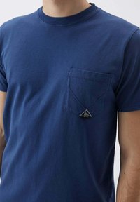 T-shirt in cotone blu navy con maniche corte, scollatura rotonda e tasca sul petto con un dettaglio a logo triangolare sul bordo della tasca.