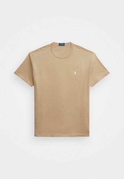 Beige bomulls t-shirt med rund halsringning, korta ärmar och en liten broderad logotyp på vänster bröst. Slät textur och enkelt design.