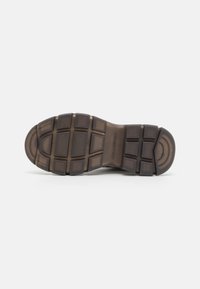 Suola di una scarpa caratterizzata da gomma testurizzata in tonalità di marrone, con un motivo a griglia e accenti circolari per una migliore aderenza.