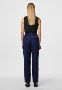 Jūras zila bikses ar augstu elastīgu jostu, divām aizmugures kabatām un taisna piegriezuma dizainu. Modelis valkā melnu bez piedurknēm topu.