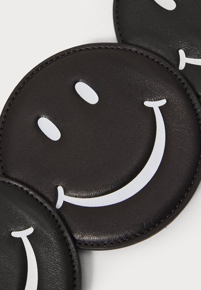Sottobicchieri in pelle nera a forma di faccine sorridenti con occhi bianchi e dettagli del sorriso. Superficie liscia e bordo cucito.
