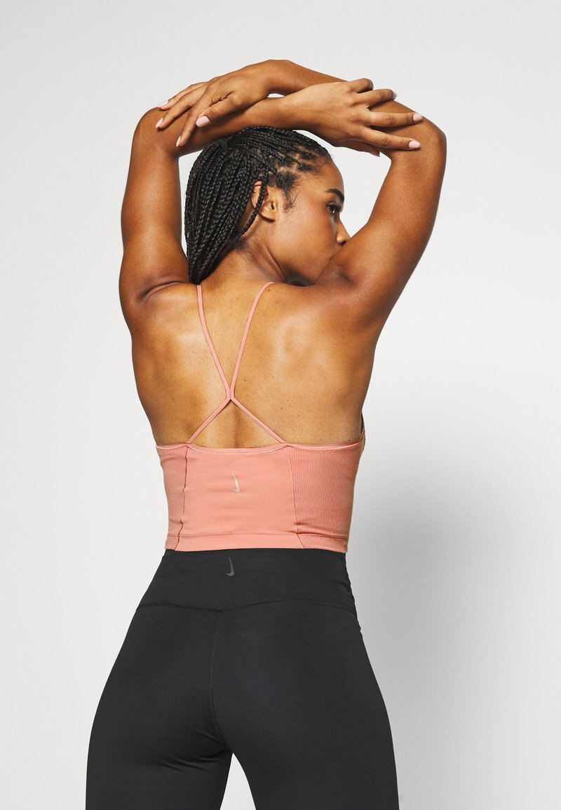 Top deportivo de rayas rosas con tirantes finos, mostrando el diseño de la espalda. Combinado con leggings negros de cintura alta, que presentan un logo sutil cerca de la cintura.