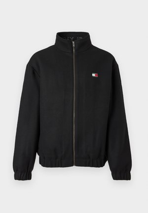 Black zip-up jacket made of soft fabric with a high collar. Features a small logo in red, white, and blue. Elastic cuffs and hem.