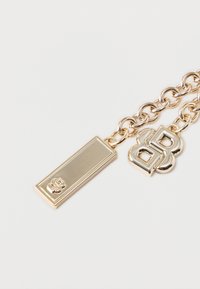 Chaîne en or avec deux pendentifs : un rectangulaire avec des initiales gravées, et un en forme d'initiales superposées sur un fond blanc.