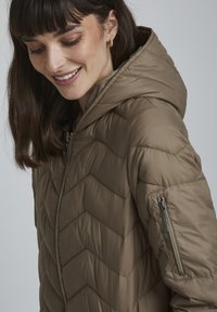 Pufová bunda v tlmenom hnedom prevedení, zdobená chevronovým vzorom, s vreckami na zips a kapucňou, vyrobená z hladkého, ľahkého materiálu.