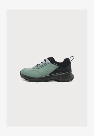 Low-Top Outdoor-Sneaker mit grünem Obermaterial, schwarzer Ferse und Sohle, schwarzen Schnürsenkeln und Zuglasche hinten.