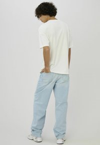 T-shirt en coton blanc à coupe décontractée, associé à un jean denim bleu clair, avec une coupe droite et des poches arrière. Baskets blanches.