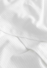 Tissu blanc côtelé avec de légers plis et ombrages, montrant la texture et les détails de couture.