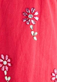 Pink fabric features three embellished flowers made of clear and pink rhinestones, with petals arranged in a decorative pattern.
