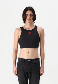 Black ribbed crop top with a round neckline and red logo detail, paired with high-waisted black jeans. Smooth texture, fitted design.