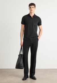 Μαύρο πόλο μπλουζάκι με κοντά μανίκια, διαθέτει τσέπη στο στήθος και λογότυπο. Συνδυασμένο με καλά ραμμένα μαύρα παντελόνια και μια μαύρη δερμάτινη τσάντα.