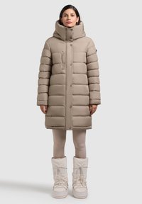 Bežs pufis mētelis ar augstu apkakli, horizontālu quiltēšanu, priekšējo pogu aizdari un sānu kabatām, kombinēts ar krēmkrāsas ziemas zābakiem.