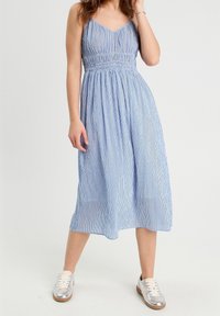 Robe mi-longue rayée bleu et blanche avec un corsage ajusté, une taille élastique et des bretelles spaghetti, associée à des baskets argentées.