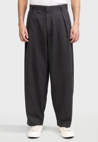 Kivikadunud hallid volditud püksid vertikaalsete triipudega, laieneva jala disain, valmistatud tekstuuriga kangast, millele on sobitatud heledad tossud.