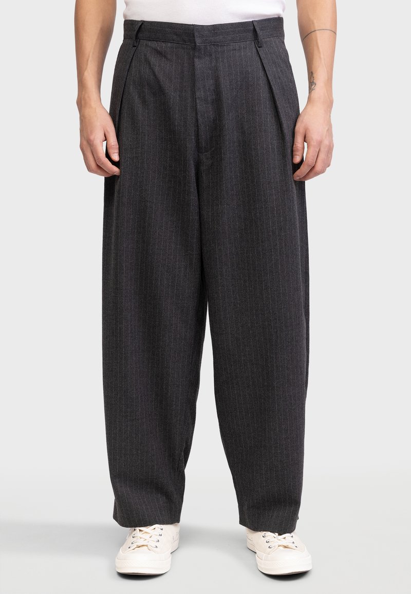 Kivikadunud hallid volditud püksid vertikaalsete triipudega, laieneva jala disain, valmistatud tekstuuriga kangast, millele on sobitatud heledad tossud.