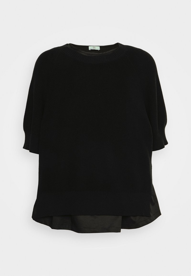 Pull en maille noire à manches courtes superposé sur un tissu noir avec un col rond et un ourlet arrière légèrement plus long sur fond uni.
