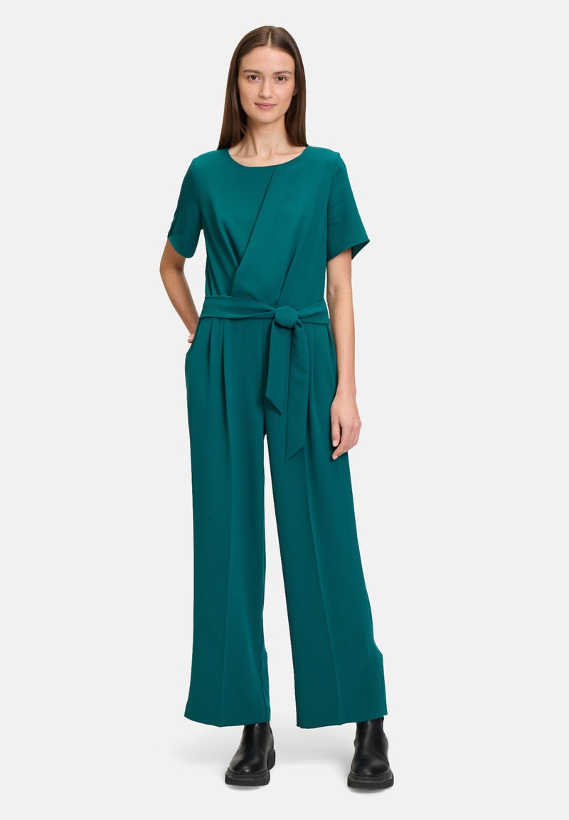 Teal jumpsuit met een relaxte pasvorm, korte mouwen, een geknoopte riem in de taille, zijzakken en wijde broekspijpen. Gladde stoftextuur.