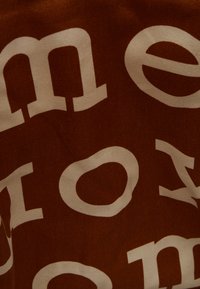 Tissu en coton présentant un grand texte blanc sur un fond marron foncé. Le design a une apparence texturée avec des éléments de typographie audacieux.