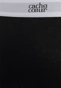 Leggings noirs avec une taille blanche sur laquelle est inscrit "cache cœur". Tissu doux et extensible avec une texture lisse. Pas de motifs ni d'accents visibles.