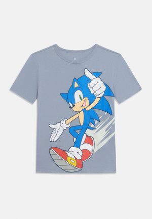 Svijetlosiva majica kratkih rukava s prikazom Sonica the Hedgehoga u trkaćem položaju s crvenim tenisicama i bijelim rukavicama na prednjoj strani.