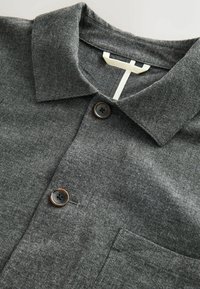 Grau gestreiftes Hemd mit strukturiertem Stoff, zwei dunklen Knöpfen und einer Brusttasche mit schlichter Gestaltung.