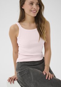 Débardeur côtelé rose clair avec un col rond, associé à un pantalon cargo ample gris foncé avec des poches latérales.