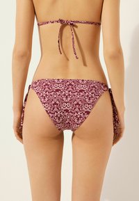 Parte inferior de bikini en burdeos con un patrón floral, con cierres laterales ajustables y cobertura moderada. Textura suave, tirantes ajustables.