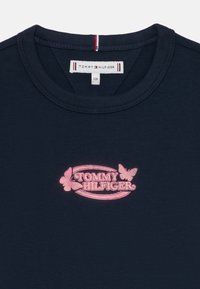 T-shirt en coton bleu marine avec un col rond et un logo brodé rose comprenant "TOMMY HILFIGER" et des papillons.