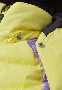 Leuchtend gelbe Jacke aus glattem Stoff mit lila Innenfutter. EnthältMetalldruckknöpfe und kontrastierende schwarze Akzente am Kragen.