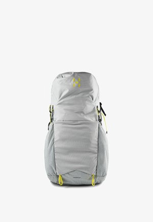 Sac à dos de randonnée gris clair avec un grand rabat, motif à carreaux sur les côtés, languettes jaunes et bretelles sur fond blanc.